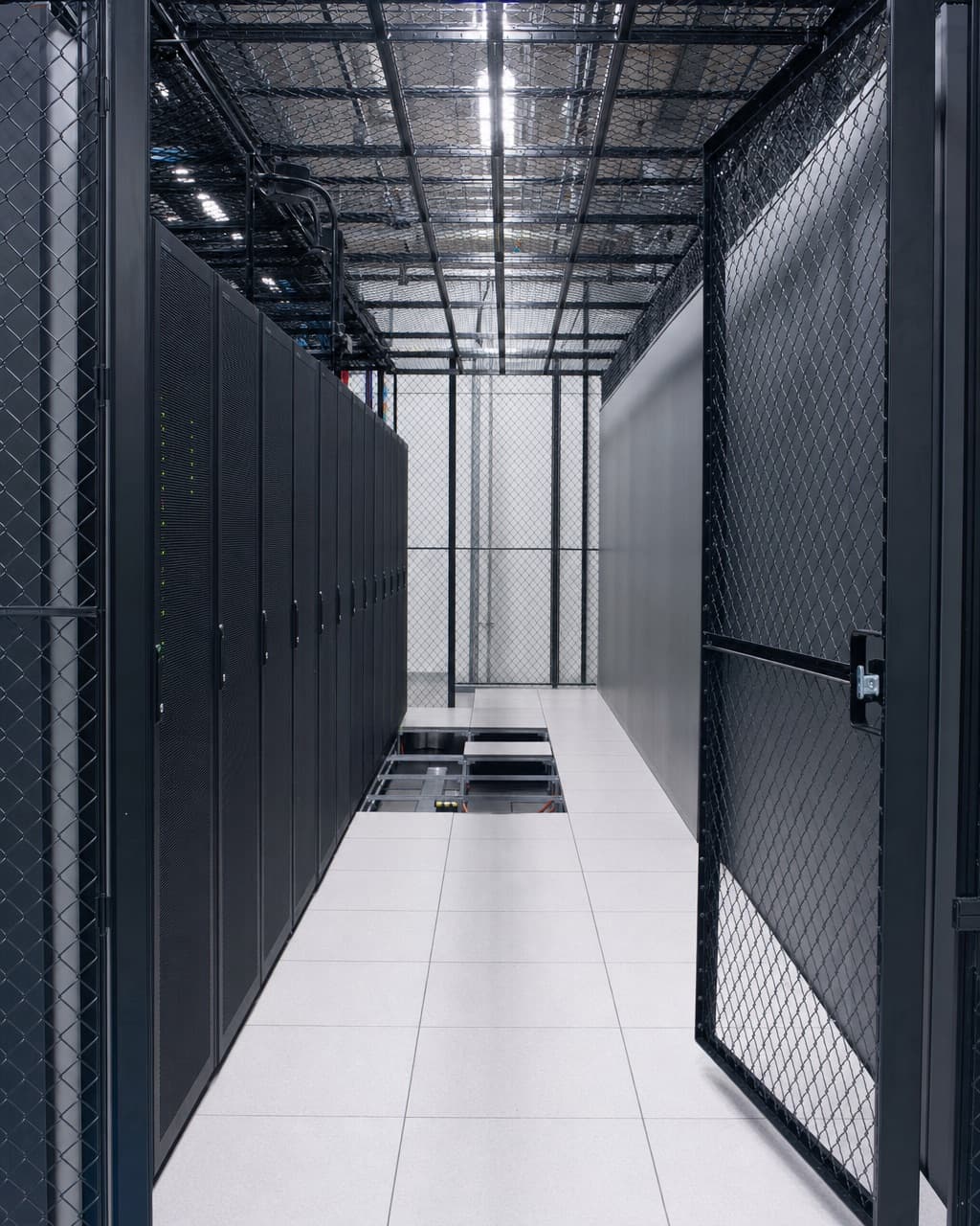 A caged colocation suite with its mesh door open, half the racks removed and floor tiles lifted at the far end